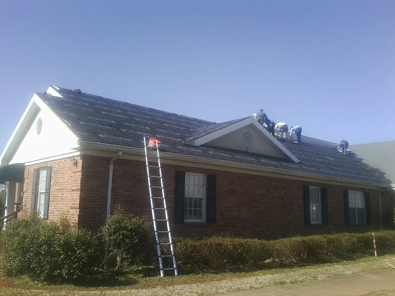 Crew tearing shingles off a brick ranch roof with a ladder set — Emergency Roof Repair work by our crew in Flushing