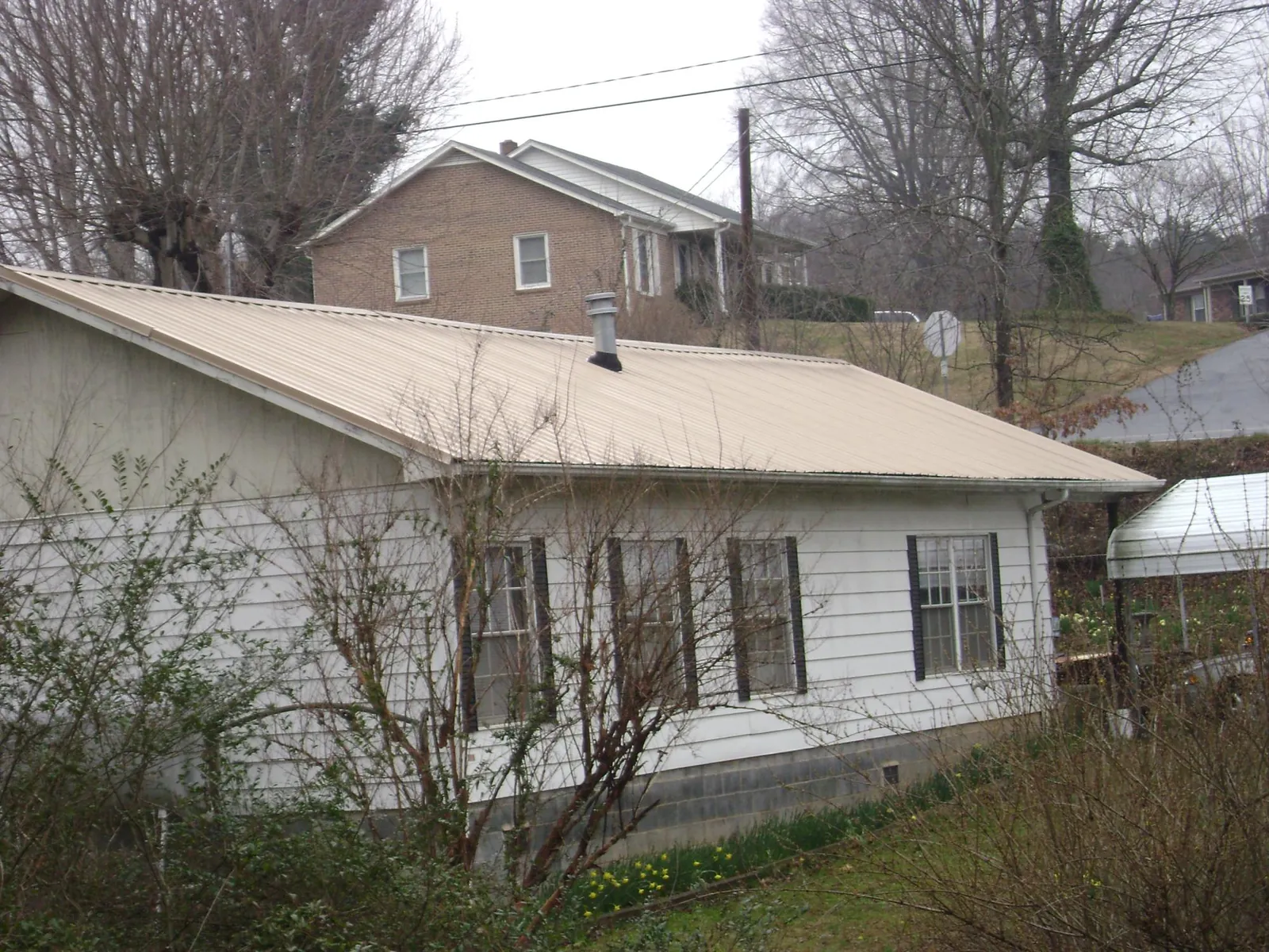 Tan metal roof on a white sided house set into a hillside — Commercial Roofing by Roofing Brothers in Flushing